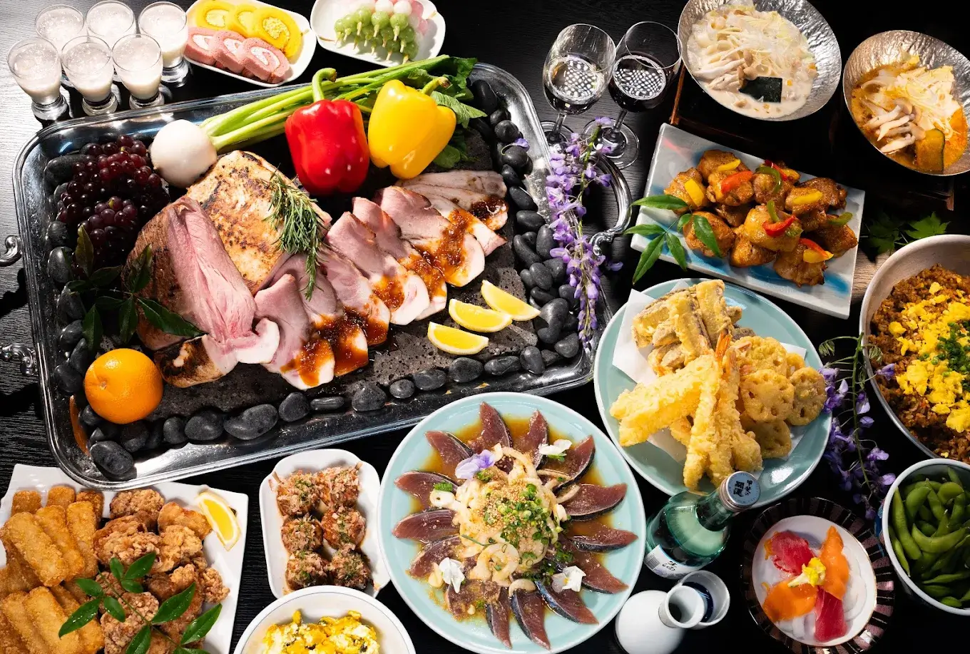 Lavish spread of sliced roasted meat with herbs, colorful peppers, grapes, lemon wedges, and assorted side dishes on a silver tray and surrounding plates.