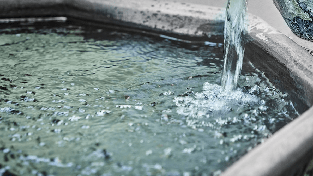 Water pours from a spout into a stone basin, creating ripples and bubbles on the surface.